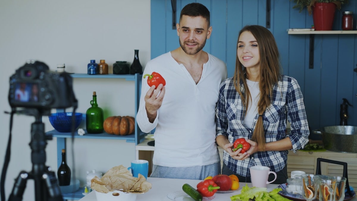 Young attractive couple recording video blog about vegetarian healthy food on dslr camera in the kitchen at home